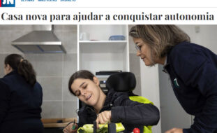 Captura de ecrã de página do sítio do “Jornal de Notícias”. Notícia com o título “Casa nova para ajudar a conquistar autonomia” acompanhada de fotografia na qual aparecem três pessoas – ao centro, sentada em cadeira de rodas, uma pessoa corta parcialmente uma curgete; à direita outra pessoa olha atentamente; ao fundo da imagem algum equipamento de cozinha e uma outra pessoa, mas de costas.