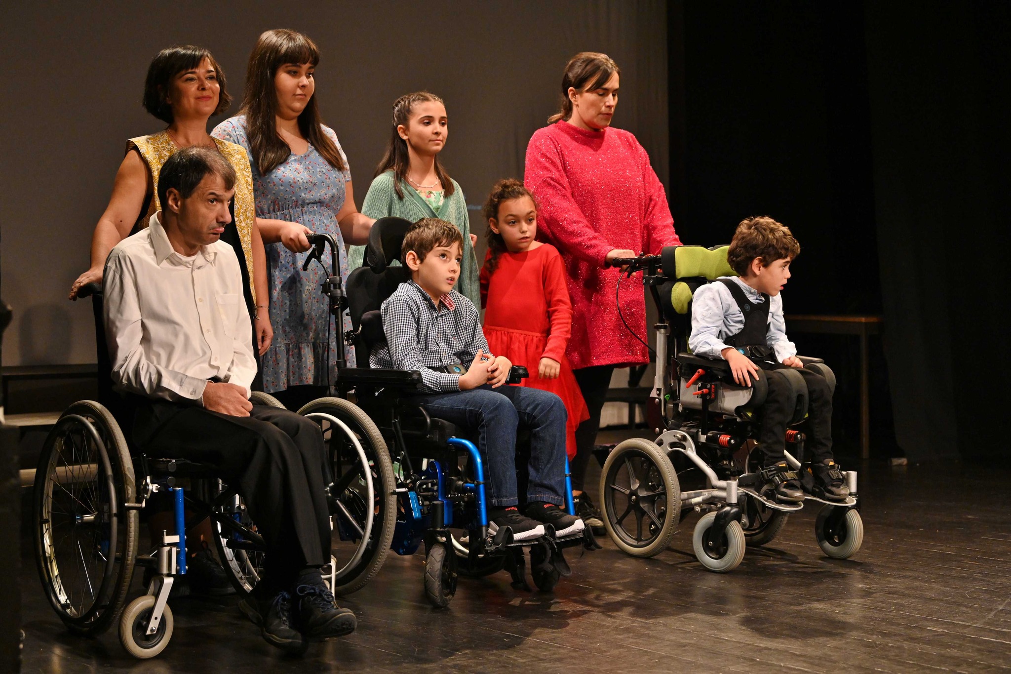 Oito pessoas em palco, sendo que três estão sentadas em cadeiras de rodas.