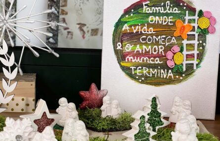 Fotografia de arranjo de Natal em cima de uma mesa. Imagens de um presépio, duas estrelas e duas árvores. Atrás um cartaz com um círculo de várias cores e a mensagem: Família, onde a vida começa e o amor nunca termina.
