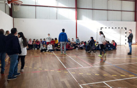 Interior de pavilhão desportivo com um vasto grupo de crianças (e alguns adultos). Os rostos das crianças foram todos desfocados.