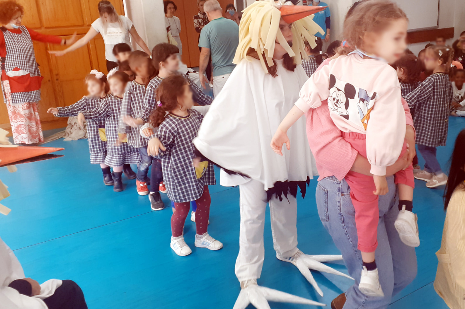 Mais de uma dezena de crianças, em fila, segue elemento do Era uma vez Teatro (caracterizado de cegonha). Ao fundo estão também alguns adultos a assistir e participar.