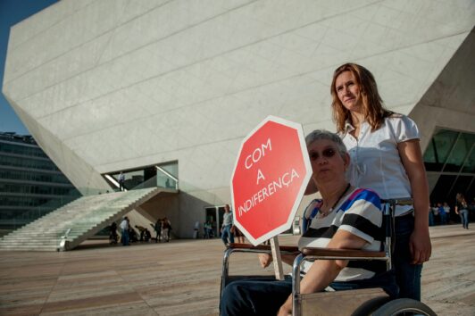 Pessoa em cadeira de rodas segura sinal de STOP com o texto branco 