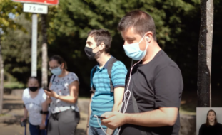 Captura de ecrã de vídeo. Várias pessoas na rua (com máscara de proteção).