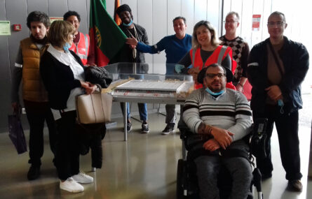 Fotografia de grupo de pessoas em sala interior. Ao fundo uma bandeira de Portugal. No centro da imagem, em cima de uma mesa, uma maquete de um edifício.