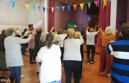 Cerca de duas dezenas de pessoas a dançar. Estão de costas, viradas para outra pessoa que, no palco, demonstra a coreografia.