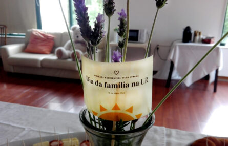 Fotografia de pequeno pedaço de papel colocado junto de algumas plantas. No papel lê-se “Dia da Família na UR”.
