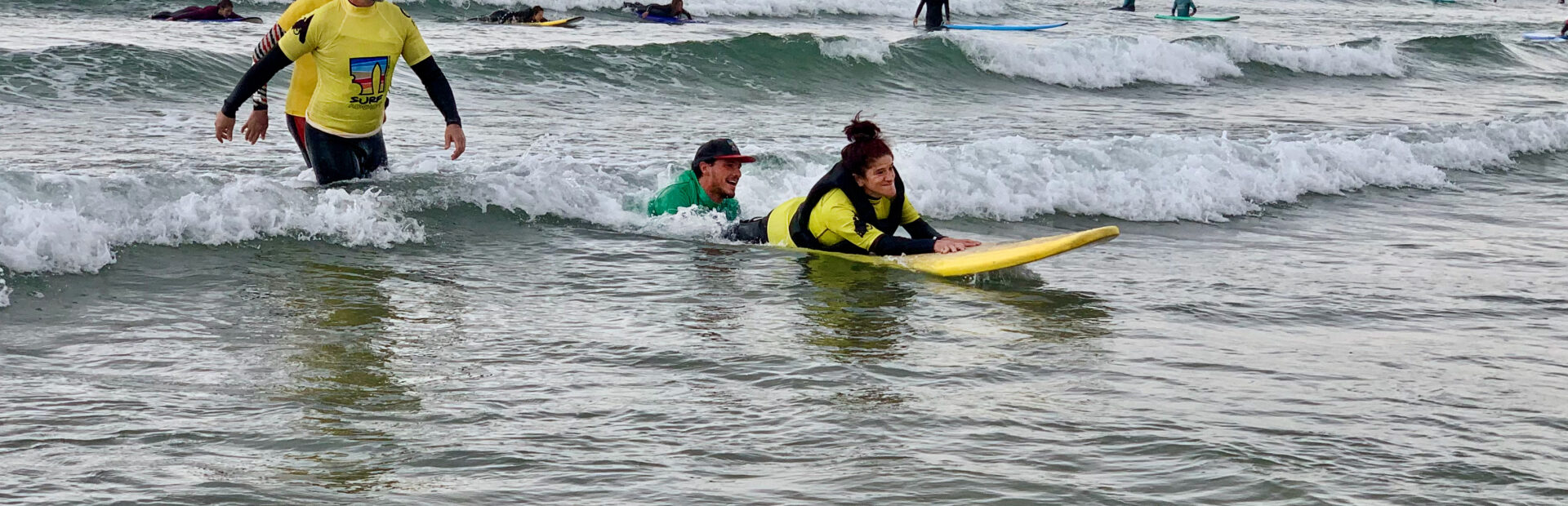 No mar uma pessoa pratica surf adaptado (estando ainda outras pessoas a prestar apoio por perto).