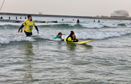 No mar uma pessoa pratica surf adaptado (estando ainda outras pessoas a prestar apoio por perto).