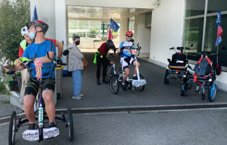 Várias pessoas testam bicicletas adaptadas. Ao lado estão ainda outros equipamentos para desporto adaptado.