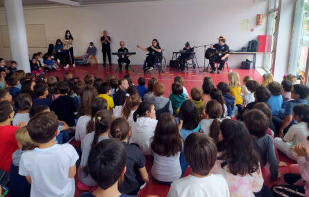 Meia centena de alunos a assistir a atuação da banda da APPC. A banda, ao fundo da imagem, é composta por quatro pessoas.