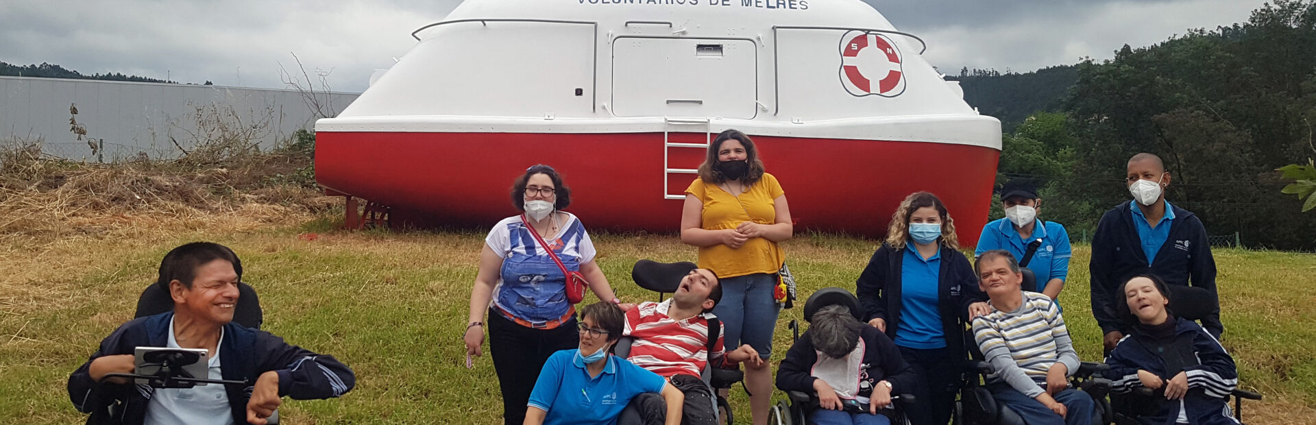 Grupo de 11 pessoas em espaço exterior. Atrás das pessoas, em zona relvada, está o que aparenta ser um pequeno barco (de apoio ou de socorro) que apresenta a inscrição “Voluntários de Melres”. Árvores ao fundo.