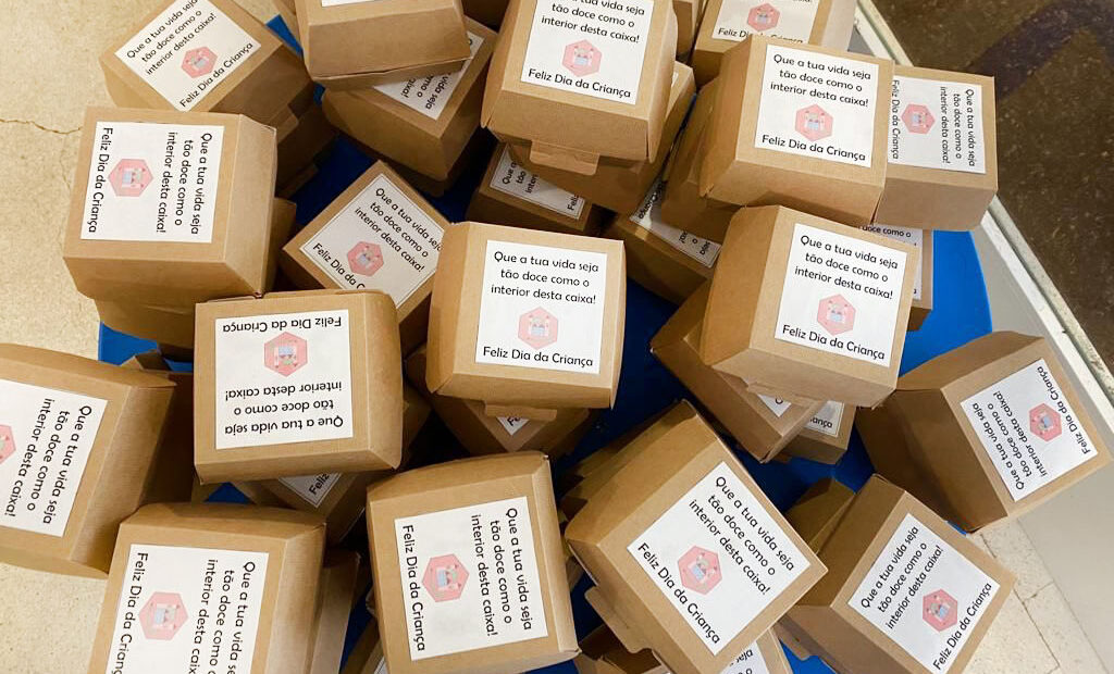 Fotografia de várias dezenas de pequenas caixas de cartão com papel colado e as frases: Que a tua vida seja tão doce como o interior desta caixa!” e “Feliz dia da Criança”.
