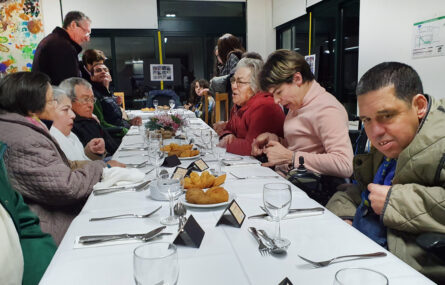 Grupo de pessoas à mesa. Além dos pratos, talheres e copos, já foram colocados alguns aperitivos.