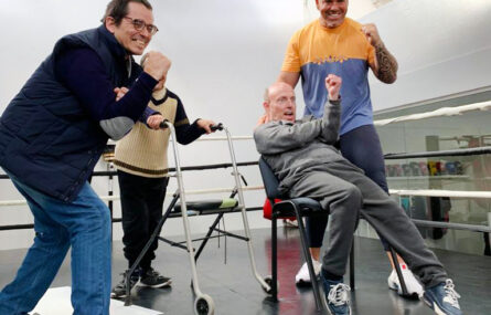 Dentro de um ringue de boxe, quatro pessoas, em distintas posições, sorriem e simulam dar murros.