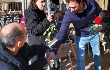 Pessoa em cadeira de rodas entrega um panfleto e uma rosa a um comerciante. Mais atrás está outro elemento do grupo de teatro a segurar um ramo de rosas.