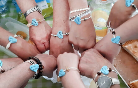 Fotografia de um conjunto de mãos todas com uma pulseira com um coração azul e vários
