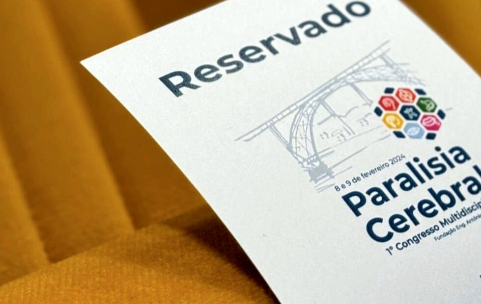 Grande plano de pedaço de papel colocado em cadeira. O referido tem impressa a palavra “Reservado” e a imagem gráfica do congresso de paralisia cerebral.