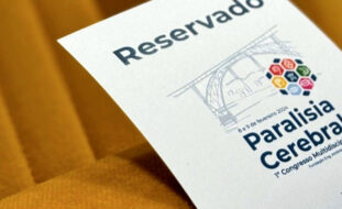 Grande plano de pedaço de papel colocado em cadeira. O referido tem impressa a palavra “Reservado” e a imagem gráfica do congresso de paralisia cerebral.