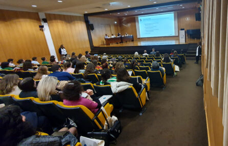 Aspeto geral do auditório com várias dezenas de pessoas sentadas. Palco com mesa e quatro pessoas. Projeção em ecrã gigante, ao centro.
