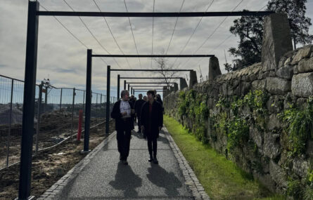 Grupo de pessoas a caminhar em percurso que é ladeado por um muro e por grades em metal.