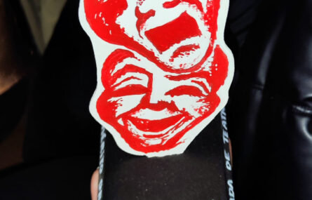 Plano aproximado de um troféu relativo à “Melhor Encenação”. O troféu tem duas imagens estilizadas relativas a teatro e apresenta a expressão “Mónica Cunha – Feitas de Ferro, Desenhadas a Carvão”.