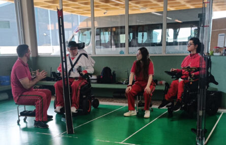 Imagem de campo de boccia (em ginásio interior). Quatro pessoas durante preparação de jogo ou treino de boccia.