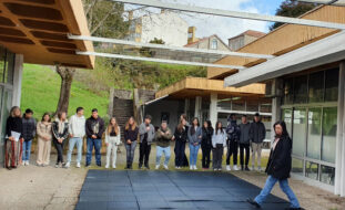 Grupo de 16 jovens lado a lado em espaço exterior. Junto deles estão três pessoas adultas. Ao fundo espaço ajardinado e alguns edifícios. Os rostos dos jovens foram digitalmente desfocados.