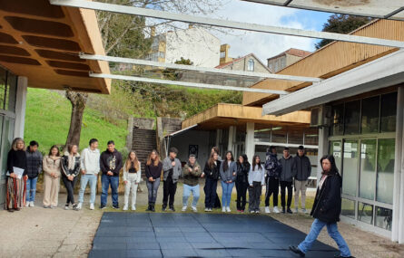 Grupo de 16 jovens lado a lado em espaço exterior. Junto deles estão três pessoas adultas. Ao fundo espaço ajardinado e alguns edifícios. Os rostos dos jovens foram digitalmente desfocados.