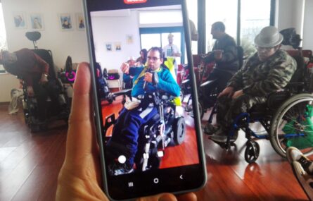 Uma mão segura um telemóvel que está a gravar um vídeo com várias pessoas.