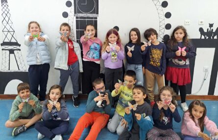 Fotografia de grupo com 14 crianças. Praticamente todas seguram uma pequena borboleta feita em papel.