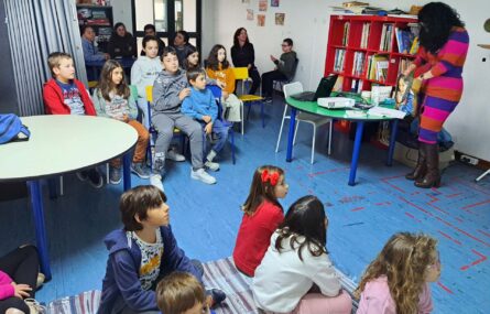 Mais de uma dezena de crianças e jovens sentados em sala interior. Parecem aguardar uma apresentação que irá ser feita por uma pessoa adulta.
