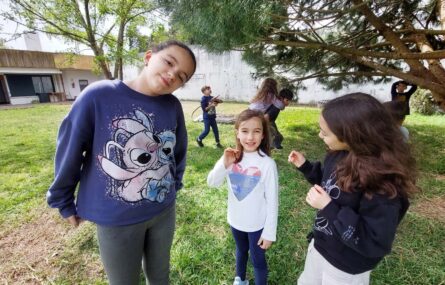 Oito crianças brincam em jardim exterior.