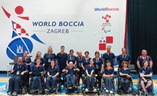Fotografia da Seleção Nacional de Boccia. Aparecem, alinhadas, 19 pessoas (em pavilhão interior e junto de um cartaz gigante com o grafismo do World Boccia Zagreb).