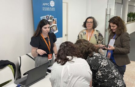 Cinco pessoas junto de uma mesa na qual está pousado um computador portátil. Mais atrás um cartaz com indicação APPC e algumas imagens.
