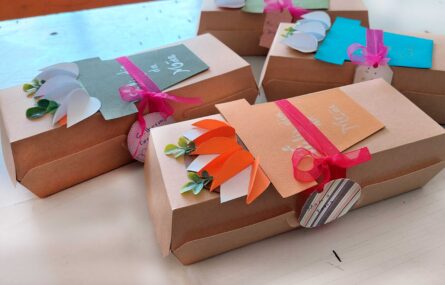 Quatro caixas em cartolina com colagens elaboradas em papel colorido. Nas colagens é parcialmente legível a mensagem “Feliz Dia da Mãe”.