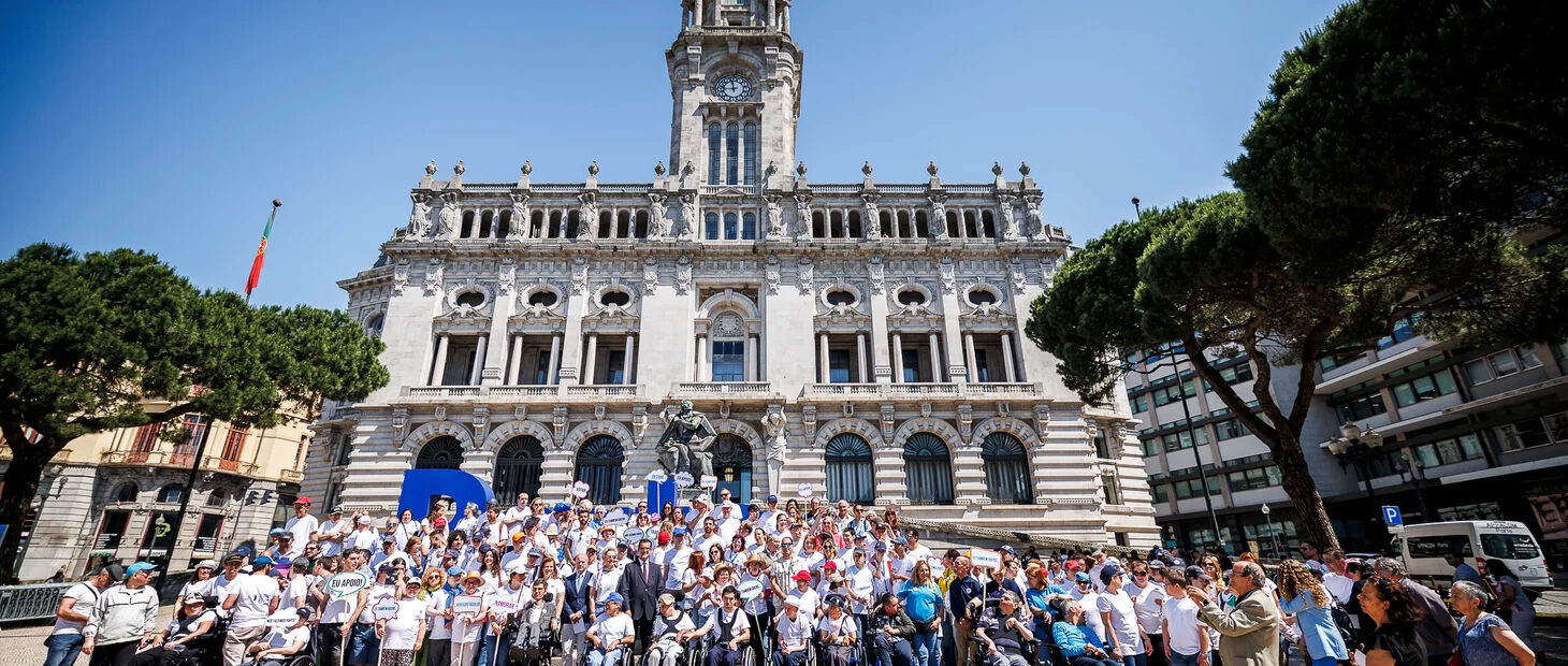 Mais de uma centena de pessoas em fotografia de grupo na praça defronte do edifício da Câmara Municipal do Porto. À esquerda e à direita da imagem são visíveis algumas árvores.