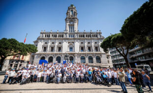 Mais de uma centena de pessoas em fotografia de grupo na praça defronte do edifício da Câmara Municipal do Porto. À esquerda e à direita da imagem são visíveis algumas árvores.