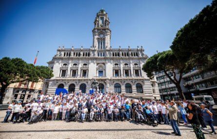 Mais de uma centena de pessoas em fotografia de grupo na praça defronte do edifício da Câmara Municipal do Porto. À esquerda e à direita da imagem são visíveis algumas árvores.