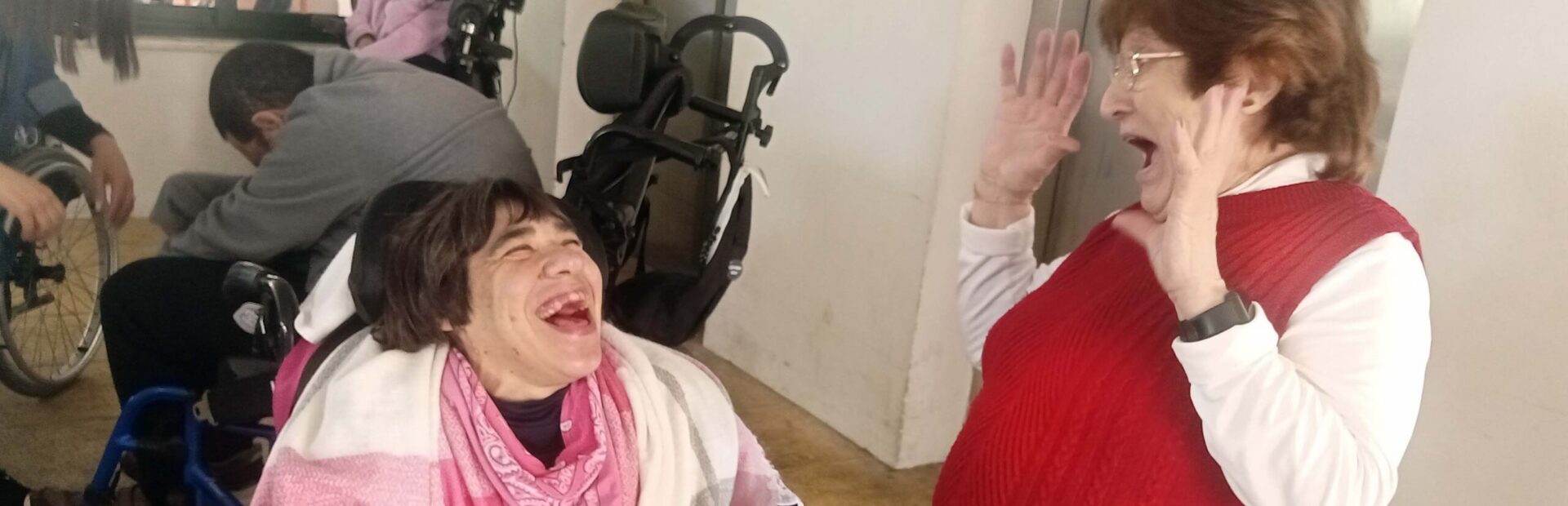 Em primeiro plano duas pessoas claramente sorridentes. Mais ao fundo outras pessoas.