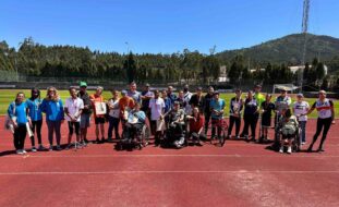 Fotografia de um grupo com 29 pessoas, lado a lado, em pista de atletismo. Ao fundo vê-se o relvado do estádio e em paisagem imensas árvores e um monte.