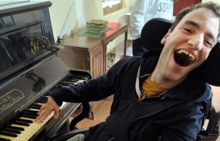 Uma pessoa sorridente aparenta estar a tentar tocar uma qualquer música num piano.