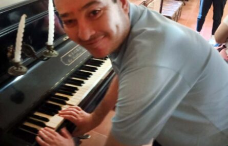 Uma pessoa sorridente aparenta estar a tentar tocar uma qualquer música num piano.