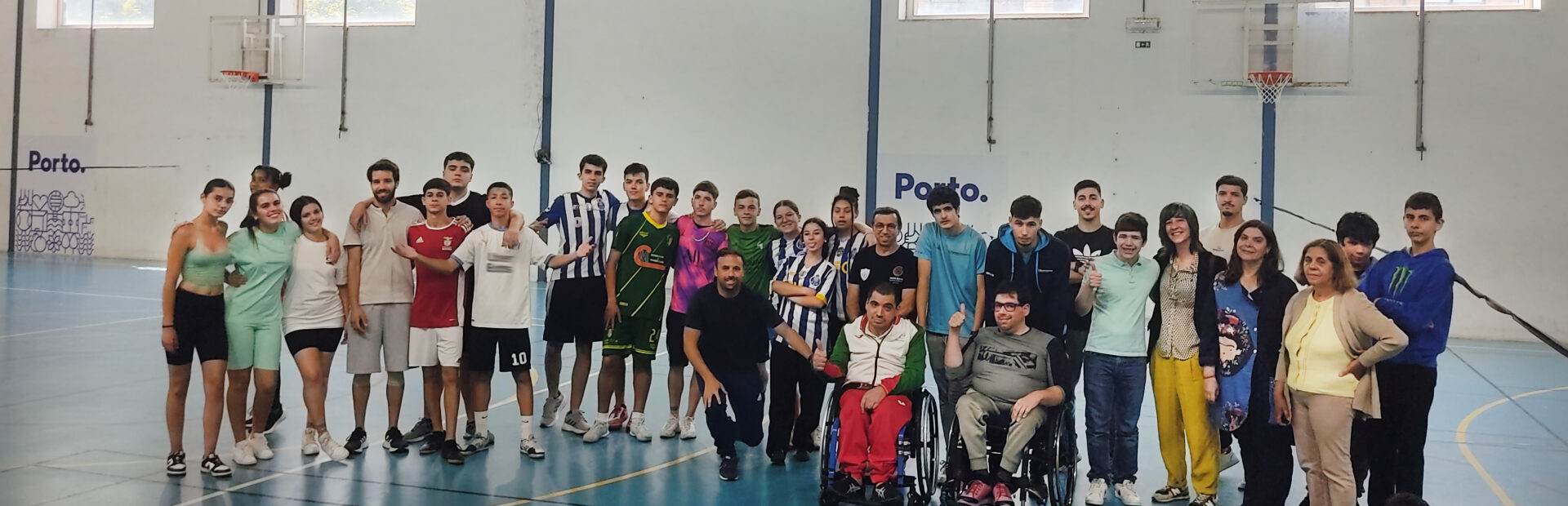 Fotografia de 31 pessoas (jovens e adultos) alinhadas em pavilhão desportivo. Duas dessas pessoas usam cadeira de rodas. À frente do grupo, sentada no chão (com as pernas cruzadas), está uma pessoa jovem. Os rostos dos jovens foram digitalmente desfocados.