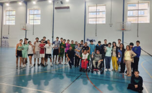 Fotografia de 31 pessoas (jovens e adultos) alinhadas em pavilhão desportivo. Duas dessas pessoas usam cadeira de rodas. À frente do grupo, sentada no chão (com as pernas cruzadas), está uma pessoa jovem. Os rostos dos jovens foram digitalmente desfocados.