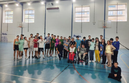Fotografia de 31 pessoas (jovens e adultos) alinhadas em pavilhão desportivo. Duas dessas pessoas usam cadeira de rodas. À frente do grupo, sentada no chão (com as pernas cruzadas), está uma pessoa jovem. Os rostos dos jovens foram digitalmente desfocados.