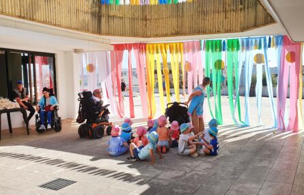 Zona exterior da APPC. Perto de duas dezenas de crianças estão junto de uma zona de acesso com fitas de plástico coloridas penduradas. Os rostos visíveis das crianças foram digitalmente desfocados.