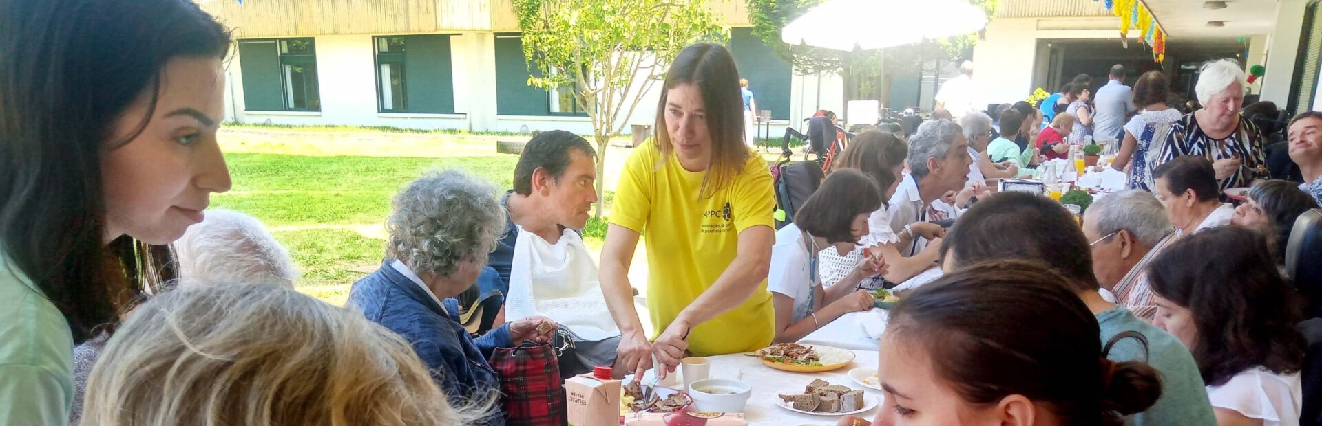 Várias dezenas de pessoas junto de inúmeras mesas repletas de comidas e bebidas.
