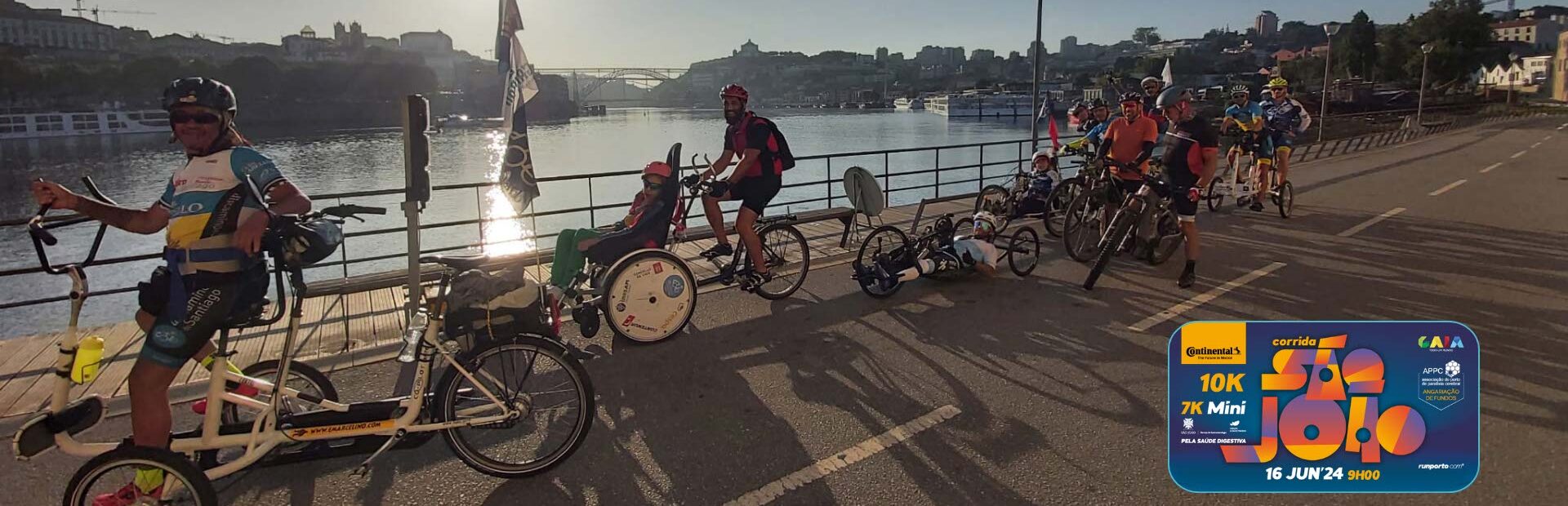 Grupo de 12 pessoas em bicicleta (normal ou adaptada) Fotografia junto do Rio Douro vendo-se do lado esquerdo parte da cidade de Gaia, à direita o Porto e, ao fundo, uma das pontes sobre o Rio Douro. No canto inferior esquerdo o logotipo da corrida.