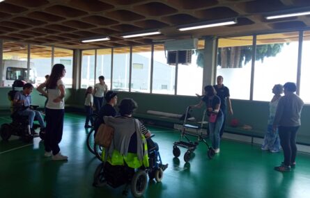 Cerca de uma dezena de pessoas em espaço desportivo interior. Não se distingue a atividade a ser desenvolvida, aparentando estarem a conversar. O rosto visível de uma criança foi digitalmente desfocado.
