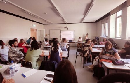 Sala interior com várias mesas e cadeiras. Cerca de duas dezenas de pessoas sentadas.